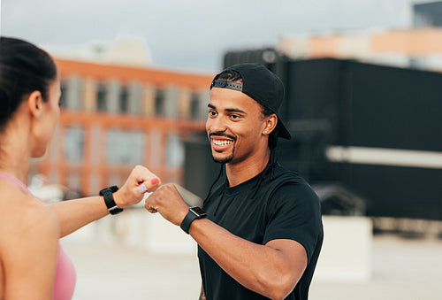 Two fitness people giving fist bumps while standing on the roof