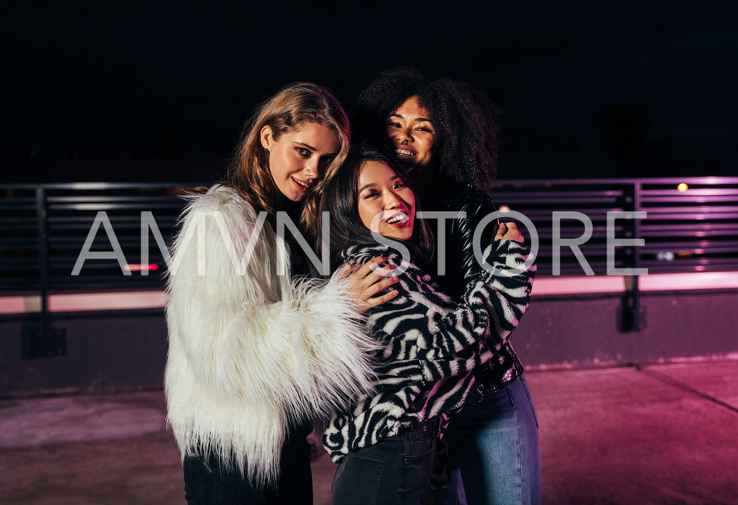 Three beautiful girlfriends embracing each other while standing on roof at neon lights	