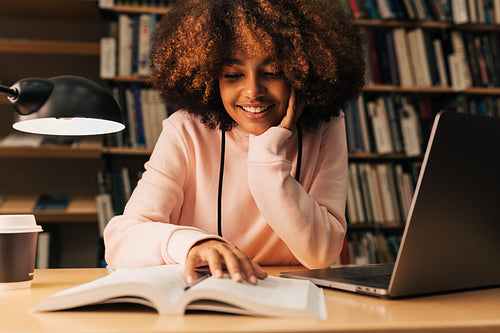 Smiling girl sitting at desk and reading in library