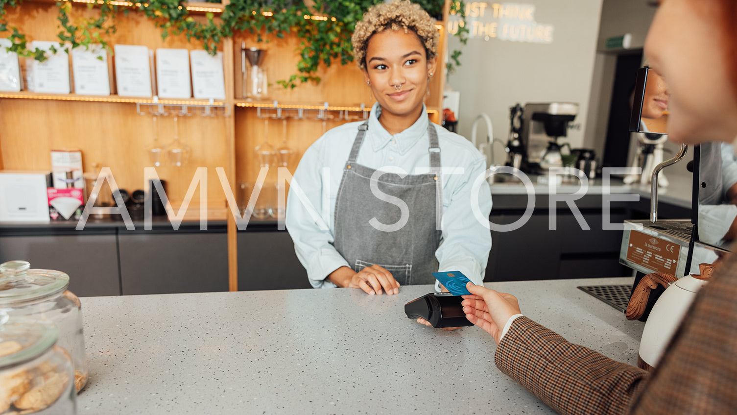 Woman bartender receives payment from a customer. Barista in apron holding pos terminal while customer paying buy card.