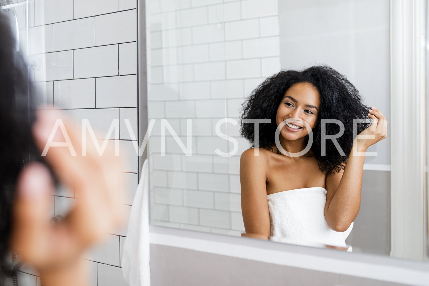 Young woman standing in bathroom, holding her curly hair	