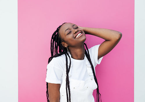 Smiling female with closed eyes adjusting her braided hair at pink wall