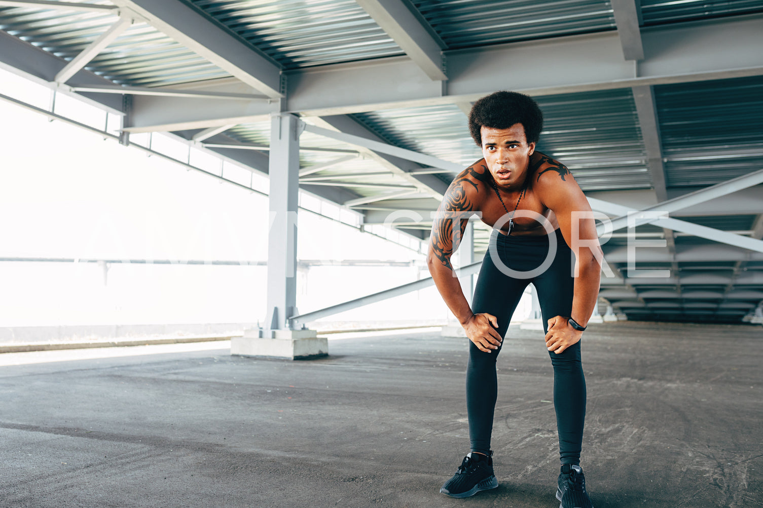 Muscular sportsman resting under a bridge with hands on his knees	