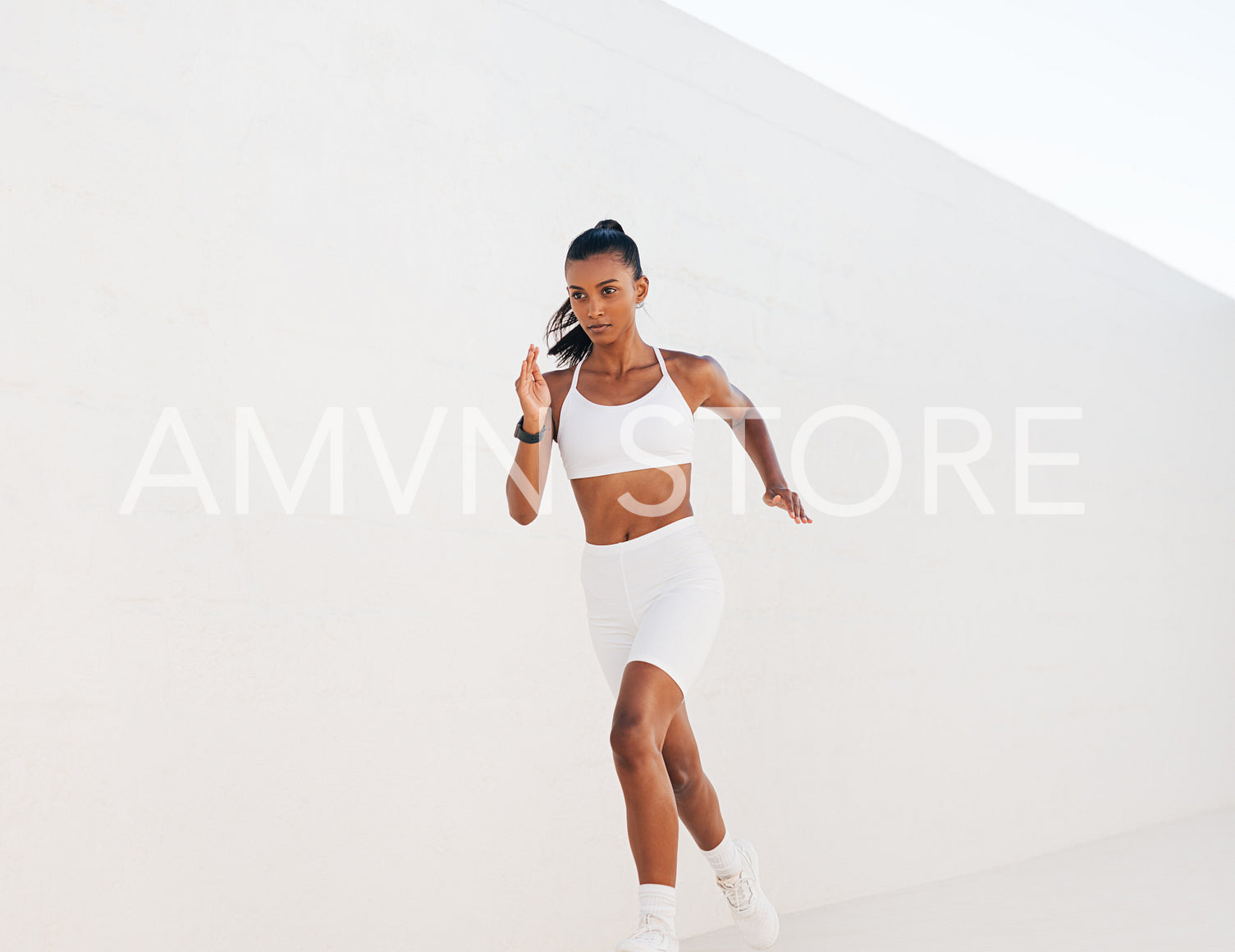 Young jogger running against a white wall outdoors. Muscular woman sprinting.