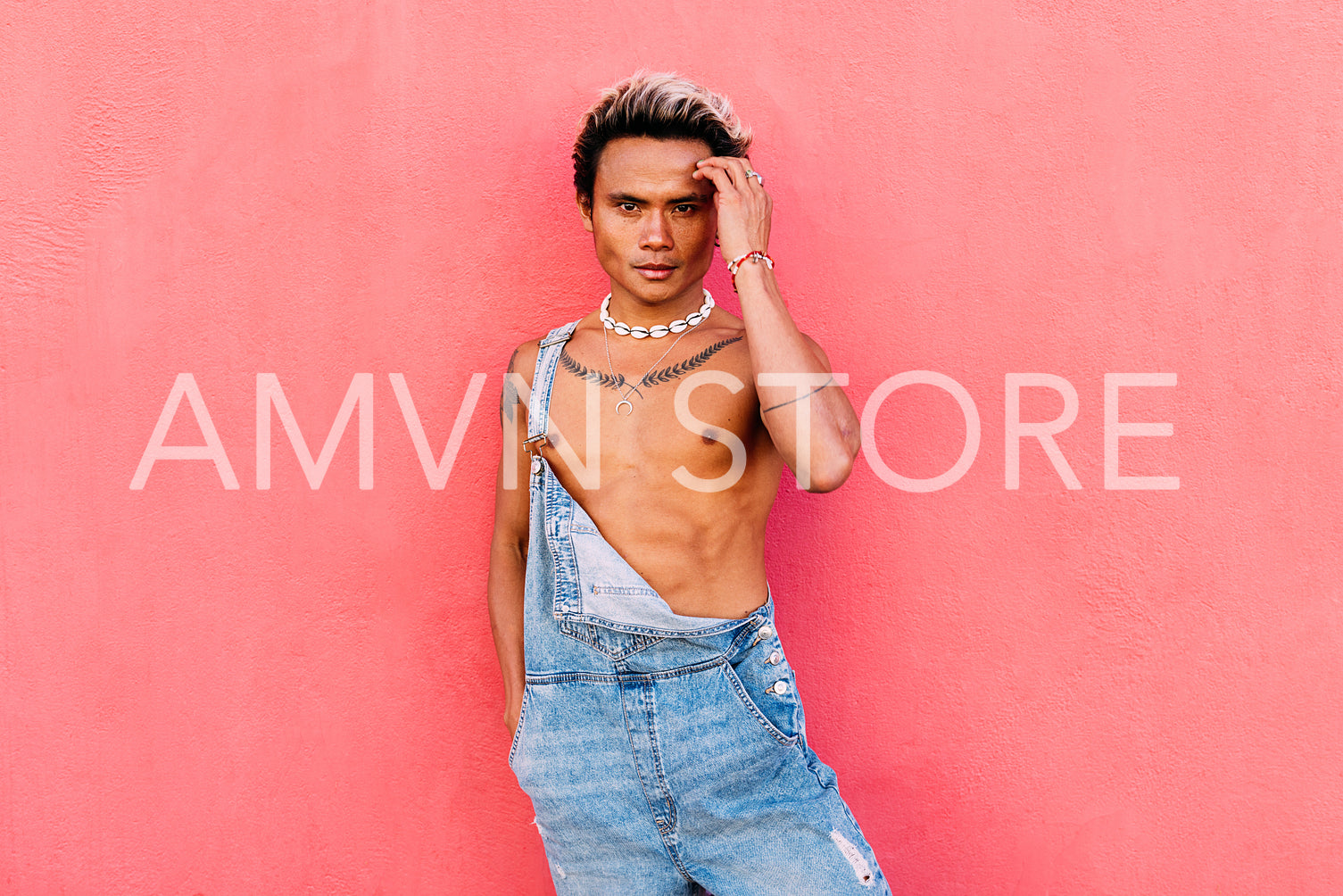 Handsome guy wearing denim overalls posing against pink background