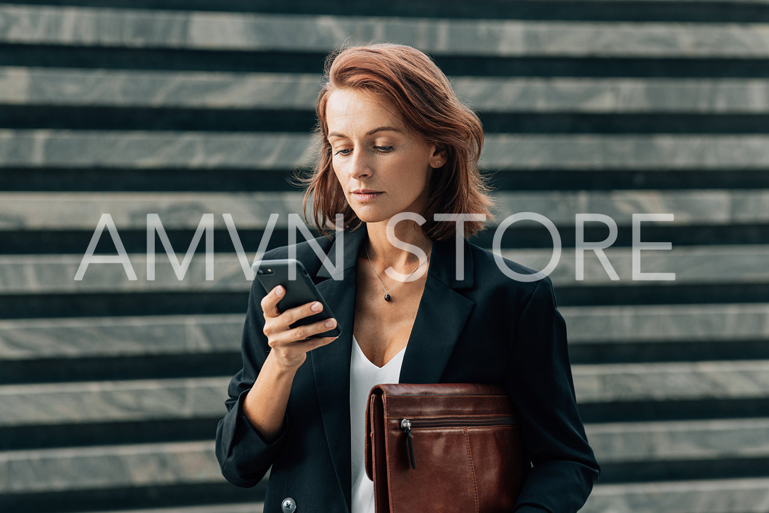 Confident middle-aged female with a leather folder looking at her smartphone while standing outdoors