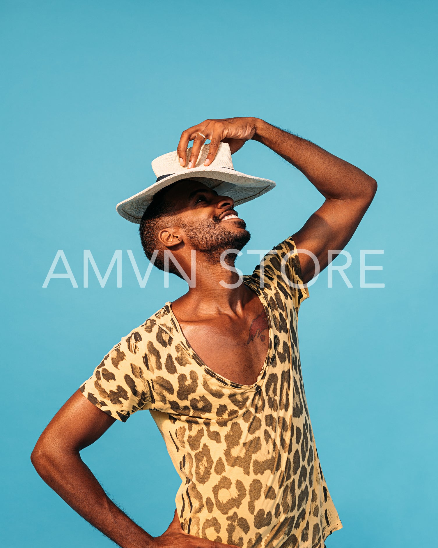 Cheerful guy in stylish clothes holding straw hat under his head in studio