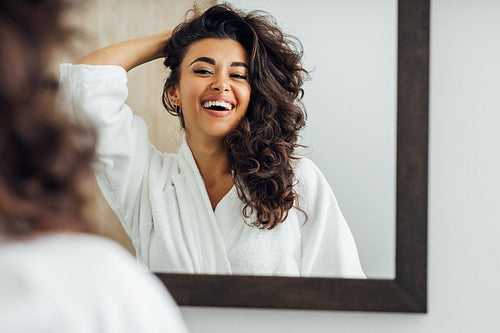 Happy woman in bathroom. Young female playing with her hair in front of a mirror.