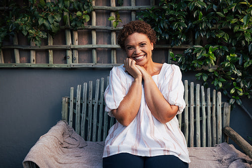 Portrait of a mature woman laughing while looking at camera. Middle aged female with short hair sitting at backyard.