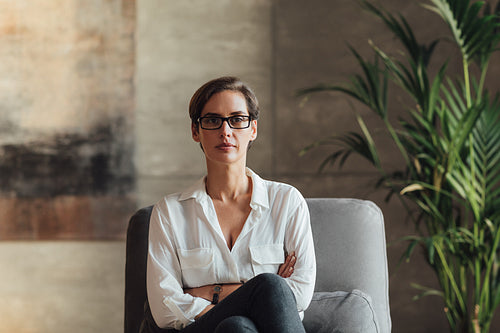 Confident female sitting in her loft. Businesswoman in eyeglasses and formal wear.