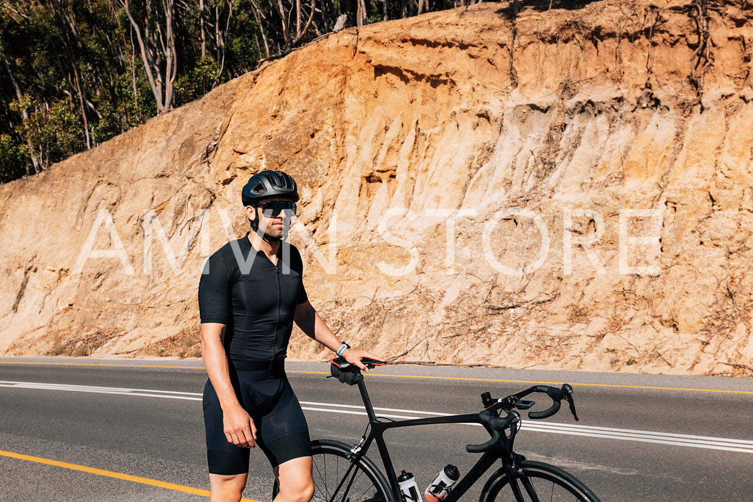 Young male cyclist in black sportswear walking on a road with his bicycle