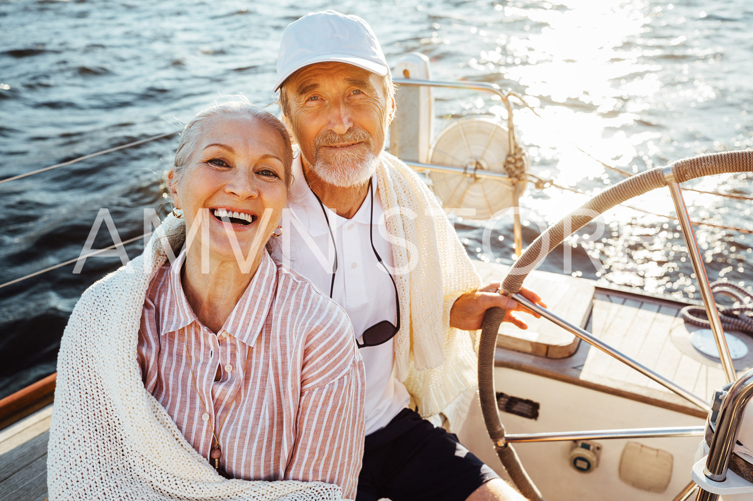 Senior couple sitting at the steering wheel on a sailboat and looking at camera	