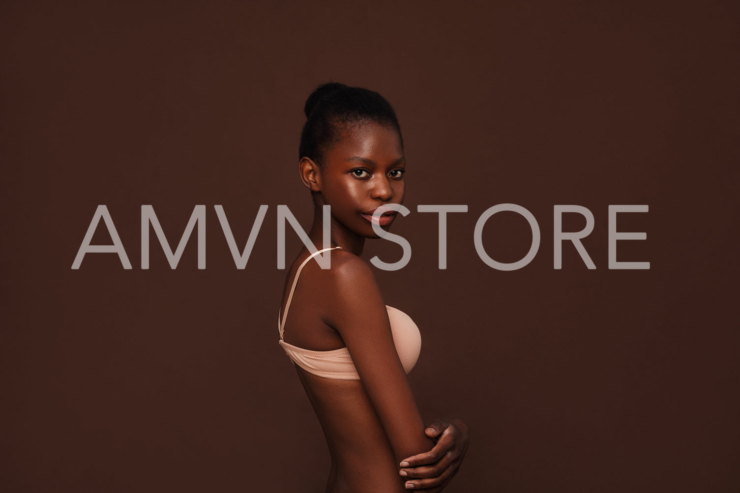 Side view of an African American girl in lingerie looking at camera against brown background