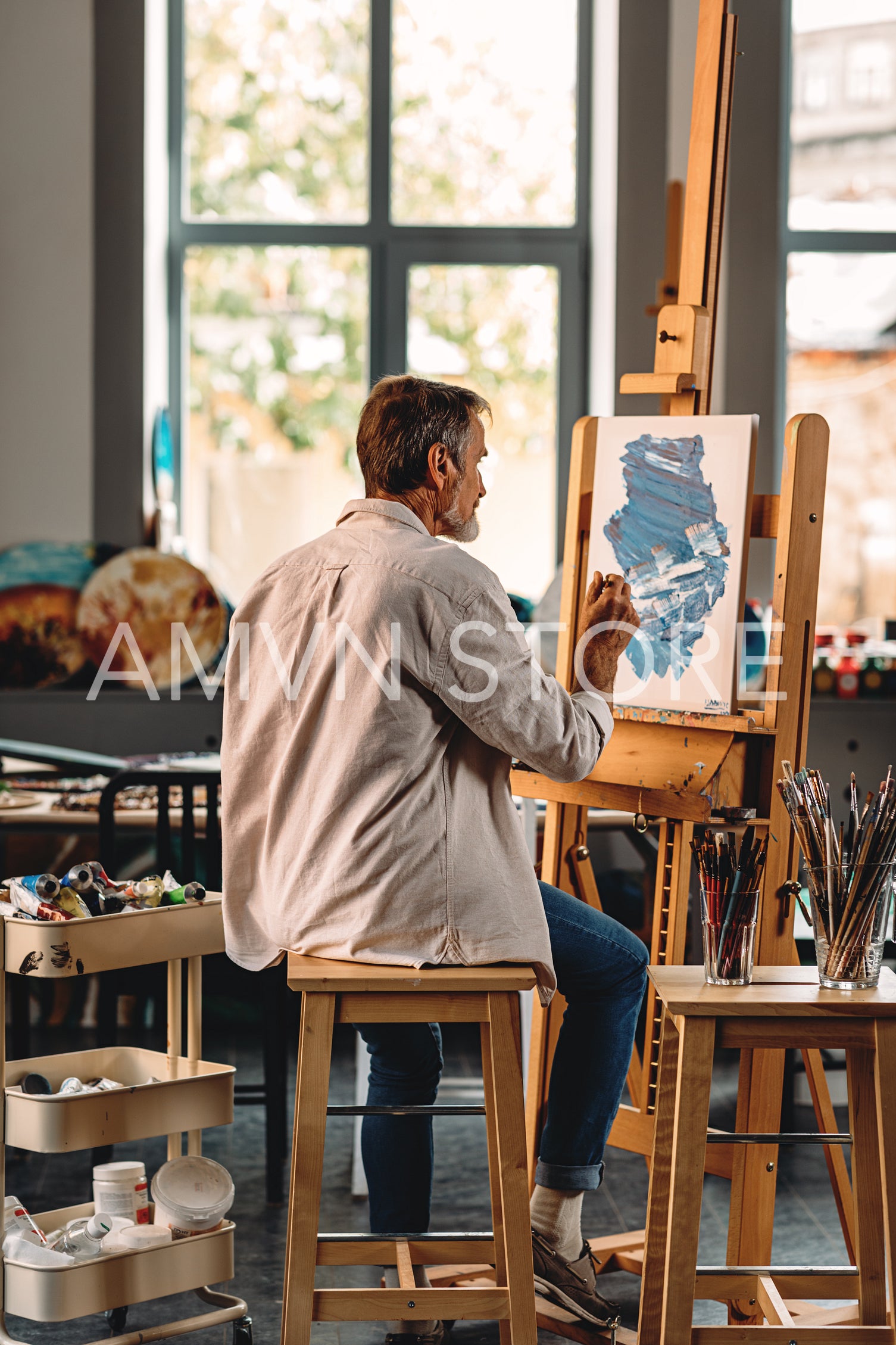 Back view of a senior artist sitting in his studio in front of an easel	