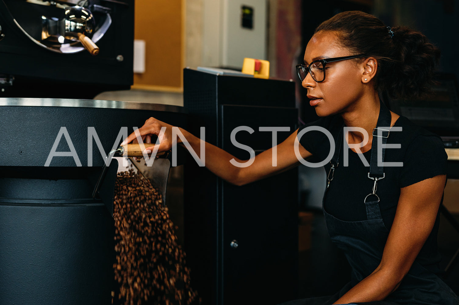 Young entrepreneur working in coffee production. Coffee beans exiting from a roasting machine.	