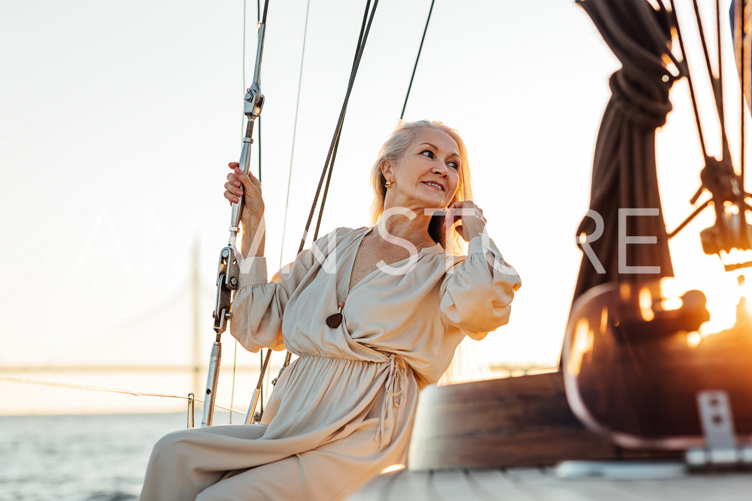 Beautiful mature woman in long dress sitting on sailboat deck at sunset and looking away	