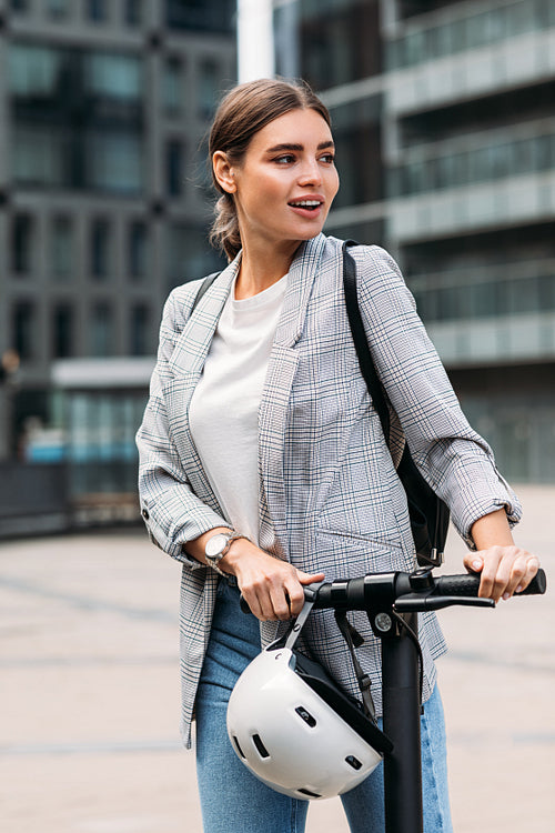 Cheerful businesswoman standing with an electric scooter in the city