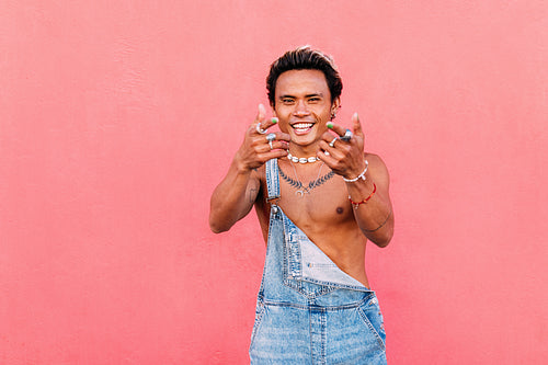 Young stylish guy in casuals dancing at pink wall and looking at camera