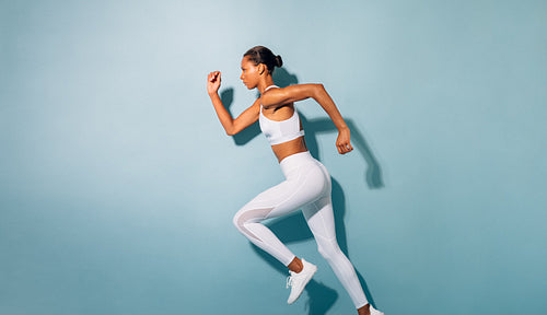 Side view of young woman running. Fitness model exercising against blue background.