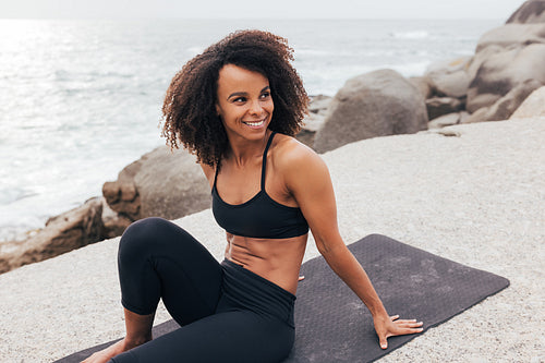 Fit woman on a mat at ocean. Slim female relaxing after yoga exercises.