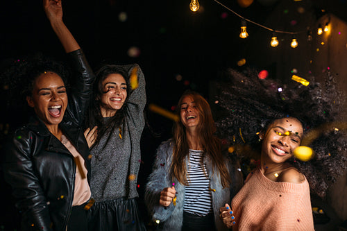 Group of female friends dancing at night under confetti