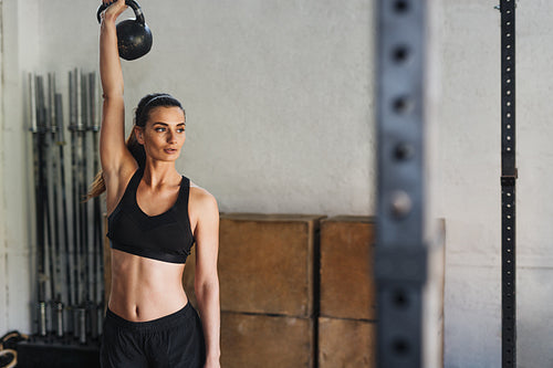 Young fitness woman lifting kettlebell at gym