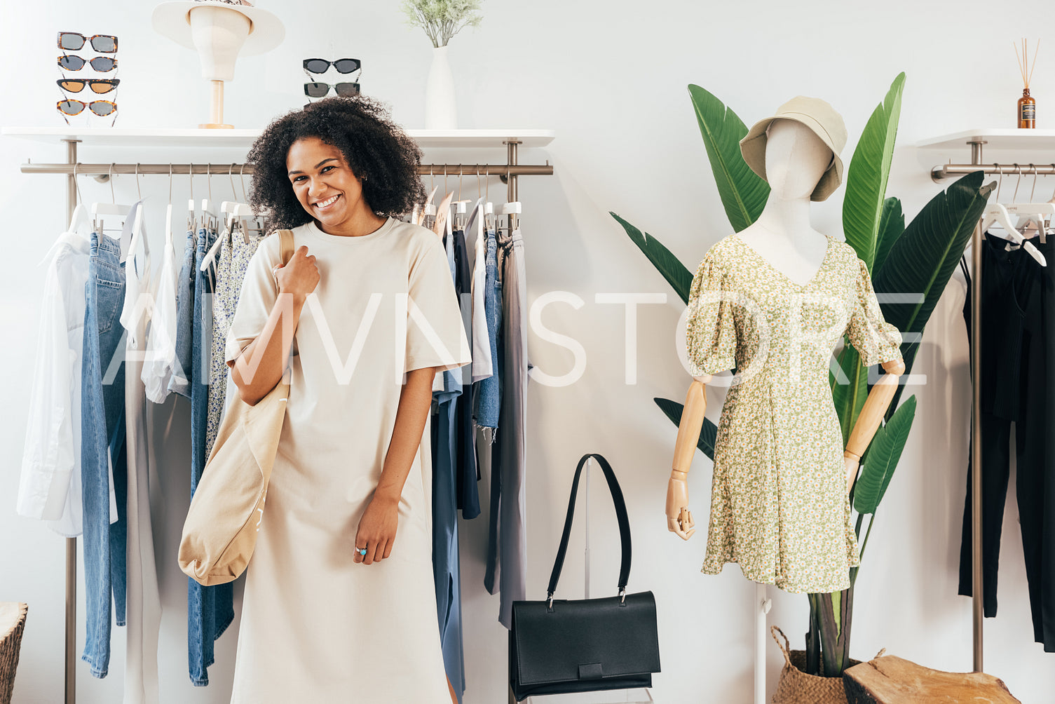 Stylish cheerful woman posing at a rack in small clothing shop looking at camera