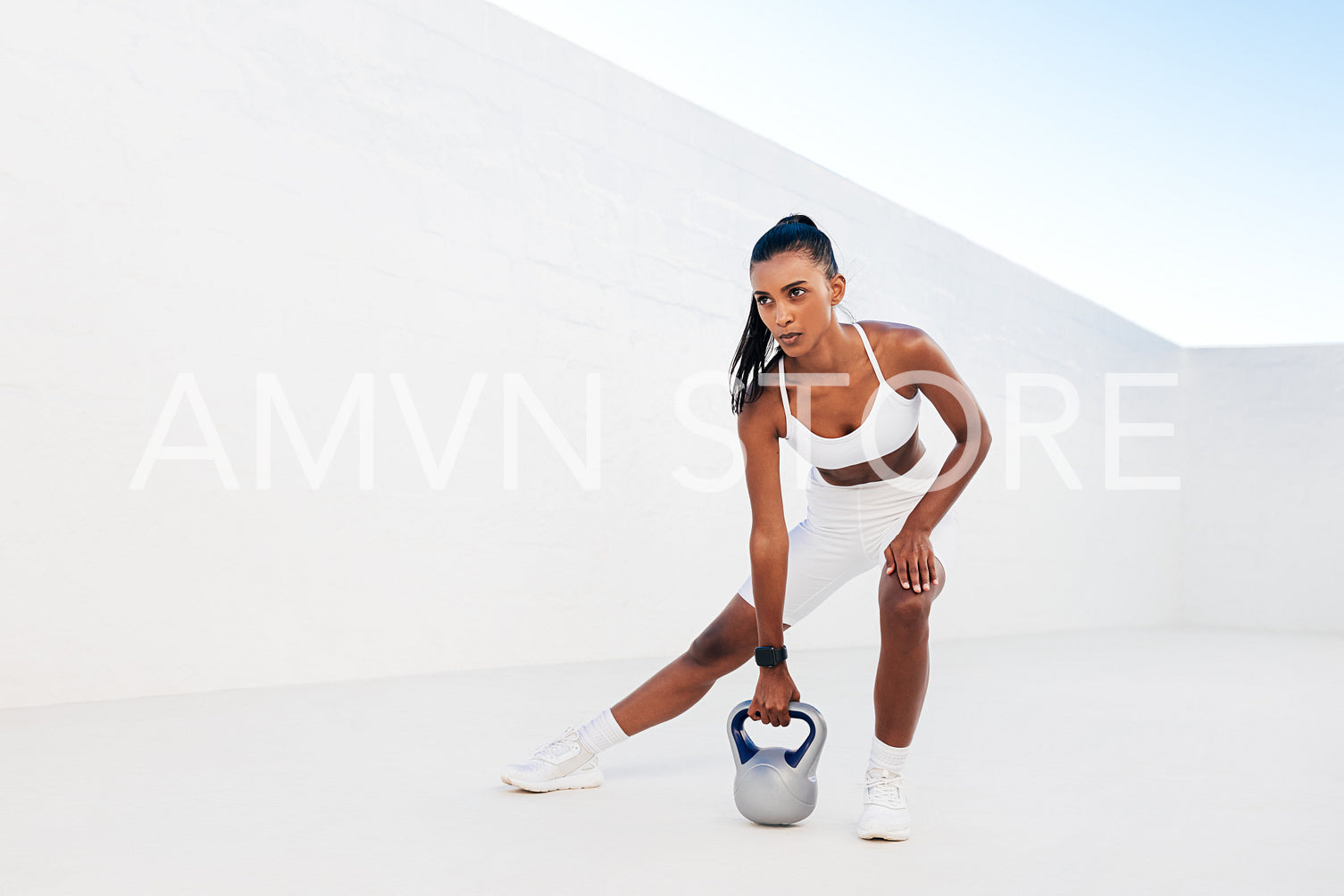 Full length of slim woman exercising with kettlebell outdoors. Professional fitness athlete doing intense training with weights in a white outdoor studio.