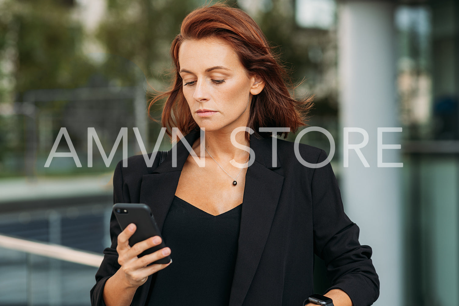 Stylish businesswoman with ginger hair wearing black formal clothes looking at mobile phone