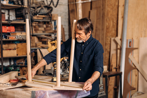 Mature carpenter measures the length of a table with a tape