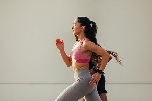 Side view of young woman runner at sunset on rooftop. Slim female sprinting with a workout buddy.