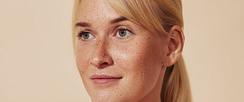 Cropped portrait of young blond woman with freckles. Female with smooth healthy skin against a pastel backdrop.