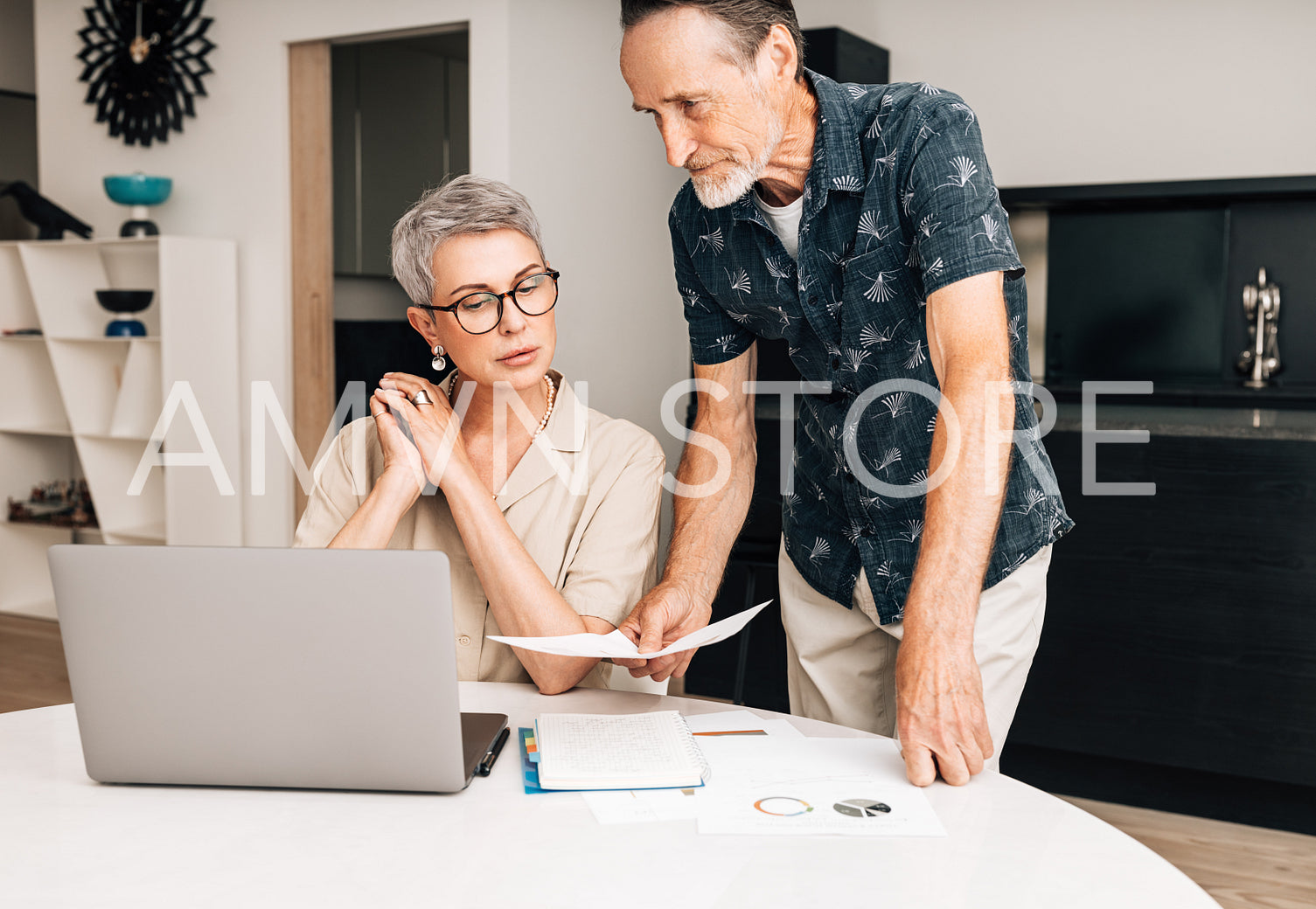 Senior couple with laptop calculating finances in the dining room. Two retired people with documents at home.