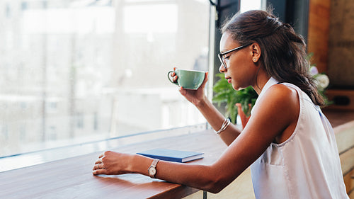 Young woman wearing eyeglasses with cup of coffee in hand and reading from digital tablet