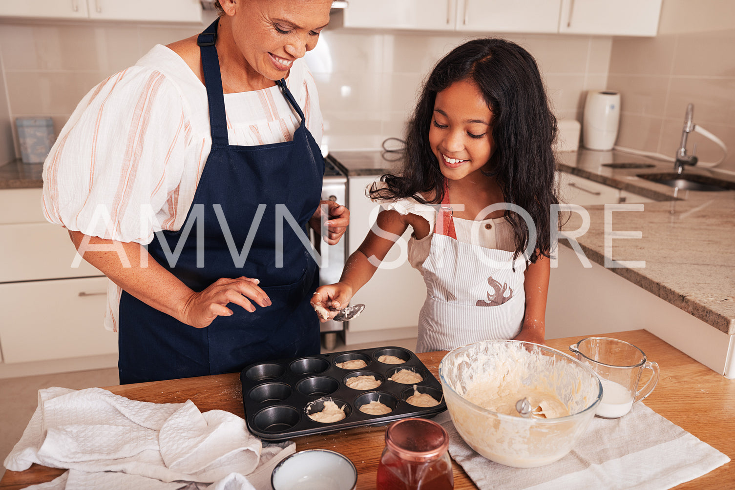 Girl in an apron pouring batter into cupcake molds while standing in the kitchen with grandma