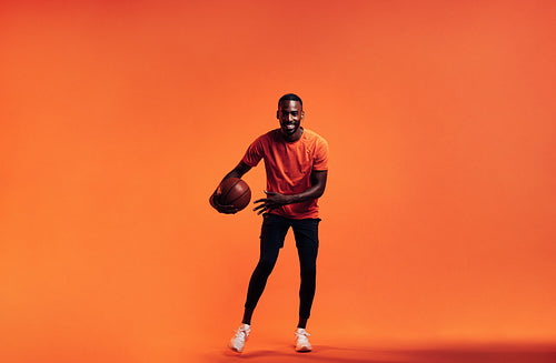 Young smiling man dribbling a basket ball over an orange background in studio