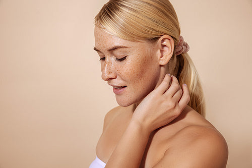 Portrait of a woman with freckles touching her neck in studio