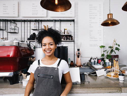 Young smiling barista wearing apron, standing at cafe counter