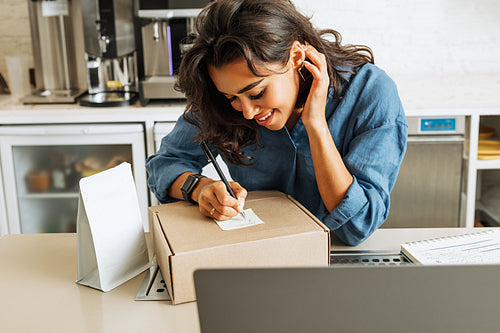 Smiling business owner taking notes on cardboard box before shipping