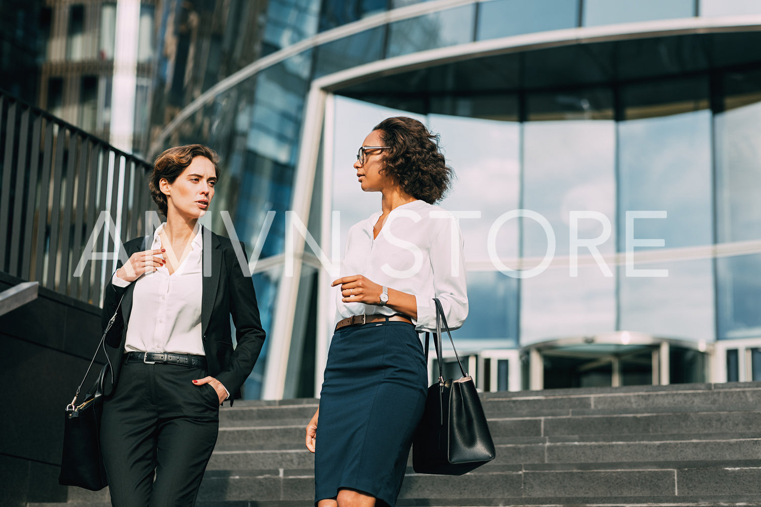 Young businesswoman discussing with her colleague while walking down the stairs near an office building	