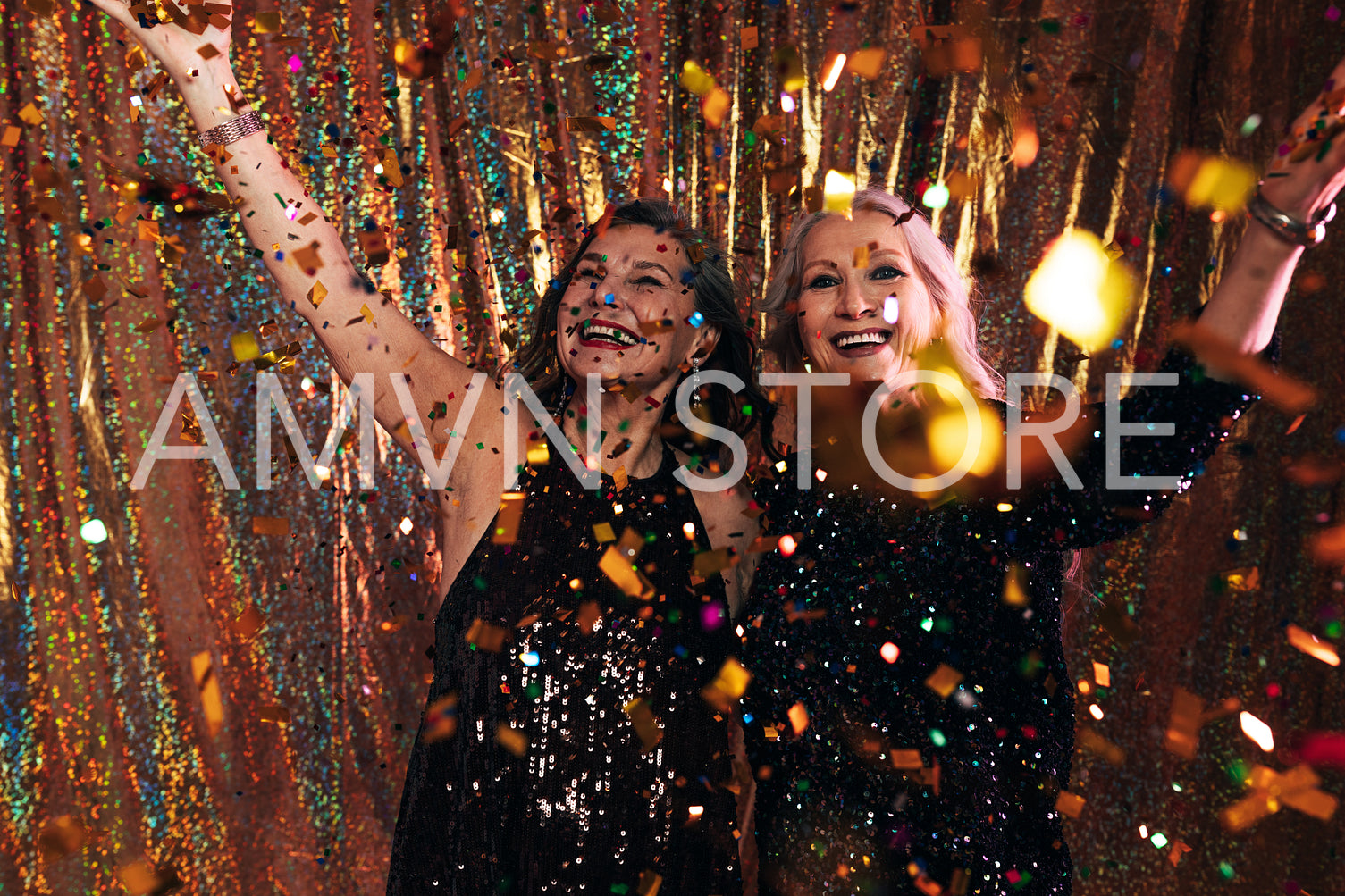 Two happy senior women in black dresses having fun under colorfu