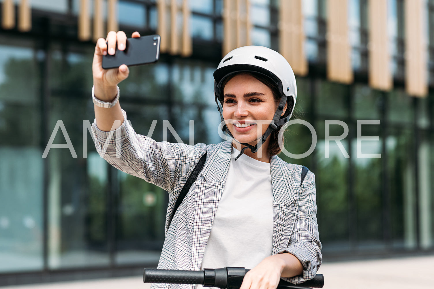 Smiling businesswoman making selfie on her smartphone while standing in the city with electric scooter