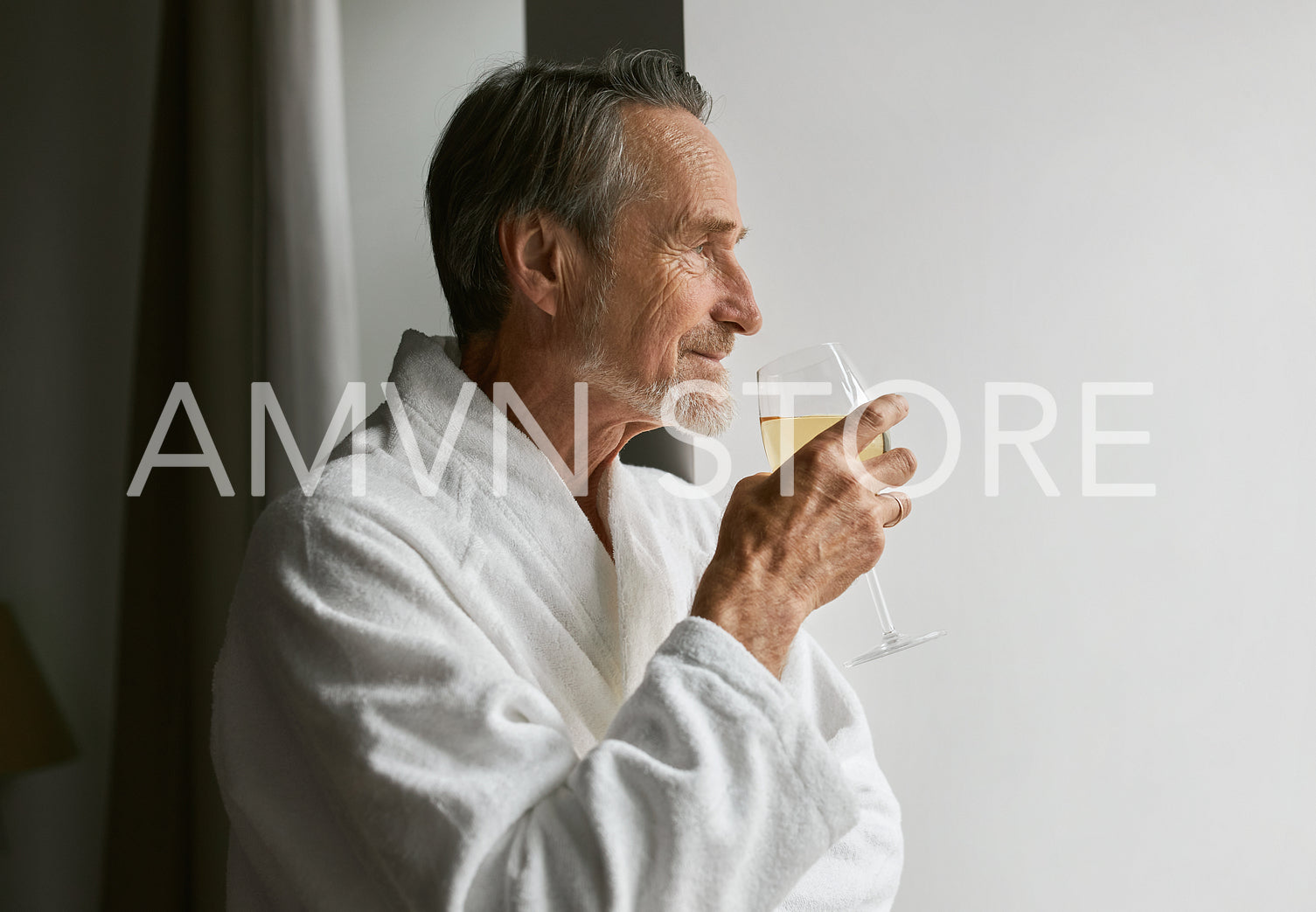 Side view of a caucasian bearded man holding a glass wine wearing bathrobe at hotel room