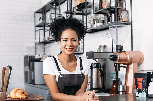 Confident barista with curly hair looking at camera standing at a counter