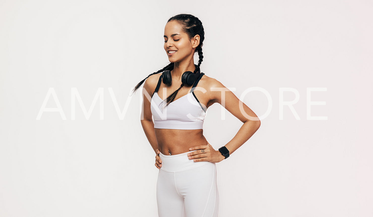 Smiling sportswoman with closed eyes standing in studio with hands on hips