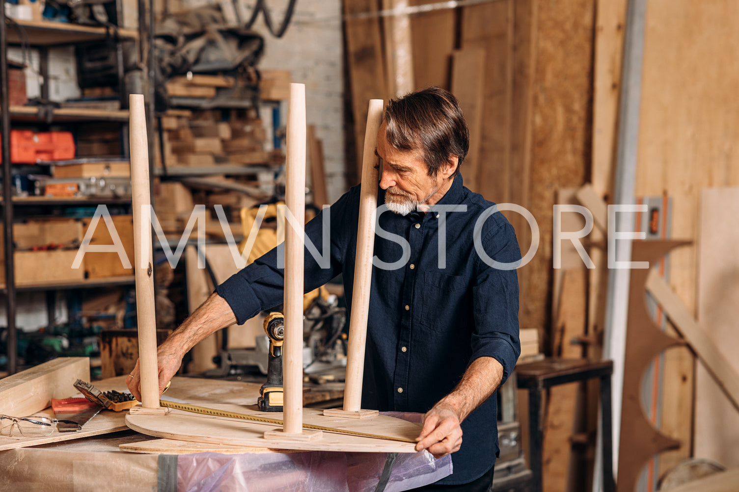 Mature carpenter measures the length of a table with a tape	