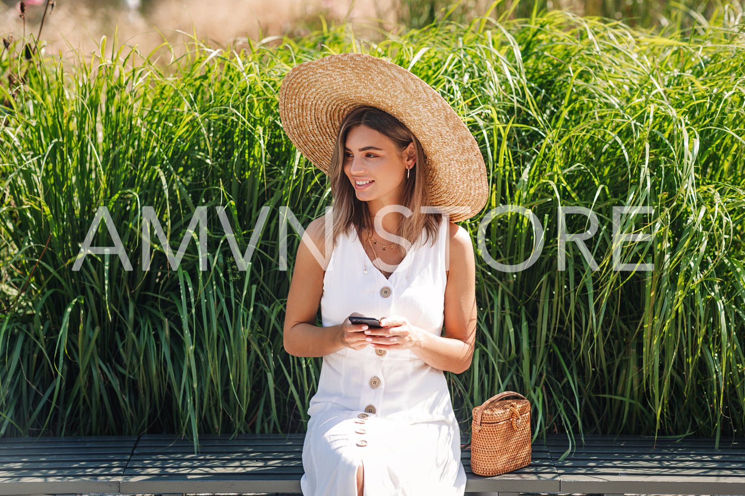 Stylish blond woman holding a smartphone while sitting in the park	