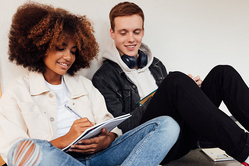 Classmates sitting at wall in high school. Teenagers preparing exams together.