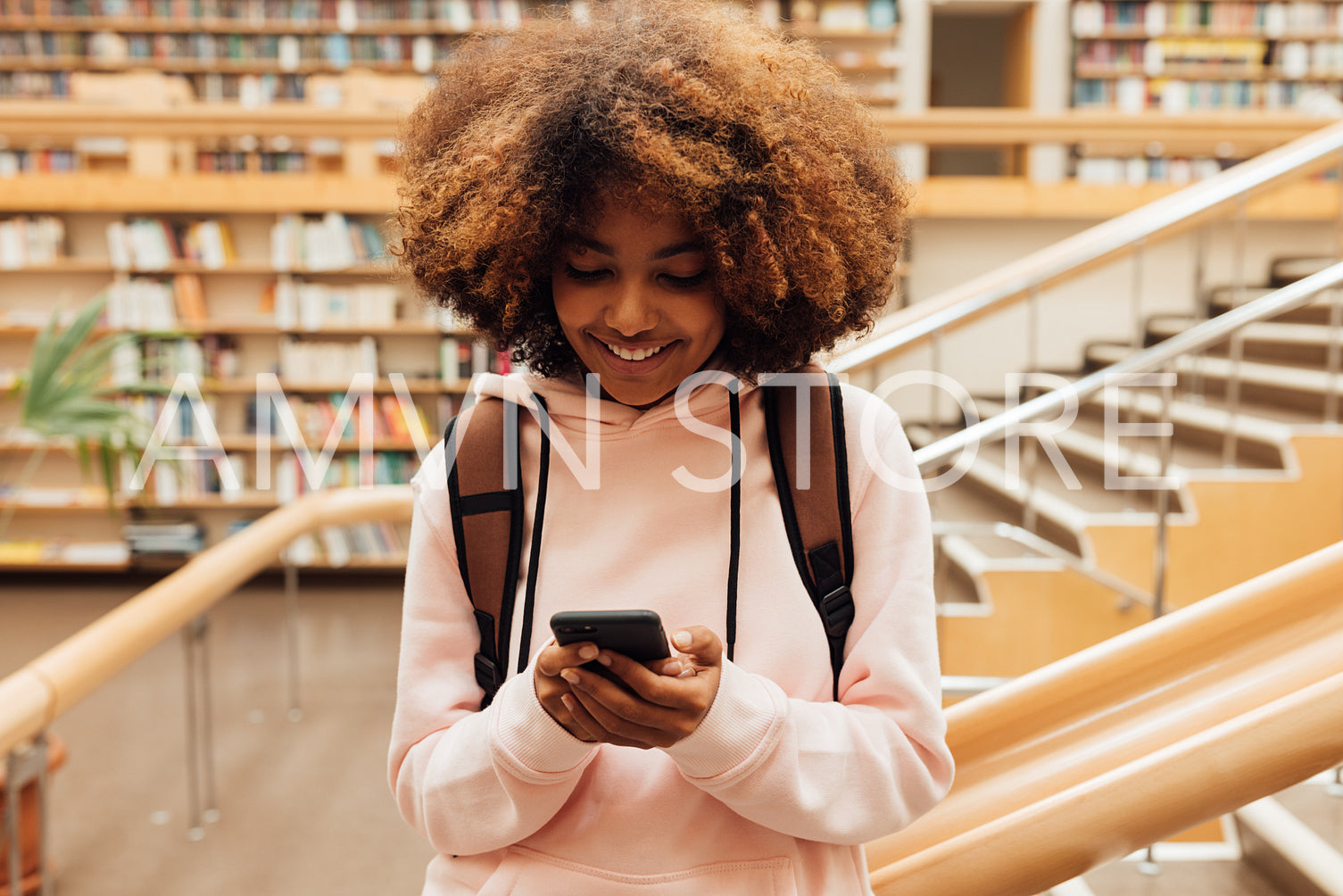 Smiling girl holding smartphone in library against bookshelf