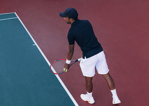 Male tennis player at baseline preparing to serve on hard court